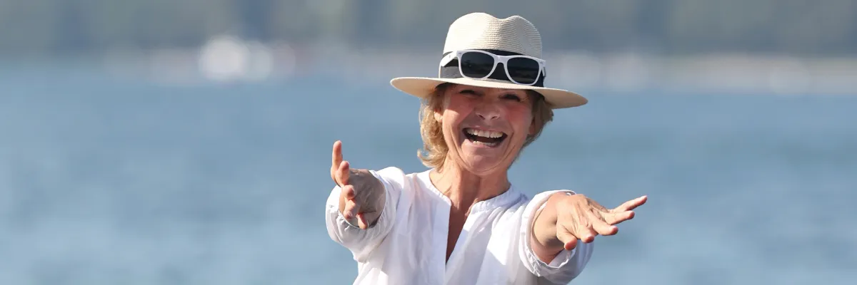 Frau mit Hut lächelt in die Kamera und streckt ihre Arme in Richtung Kamera aus