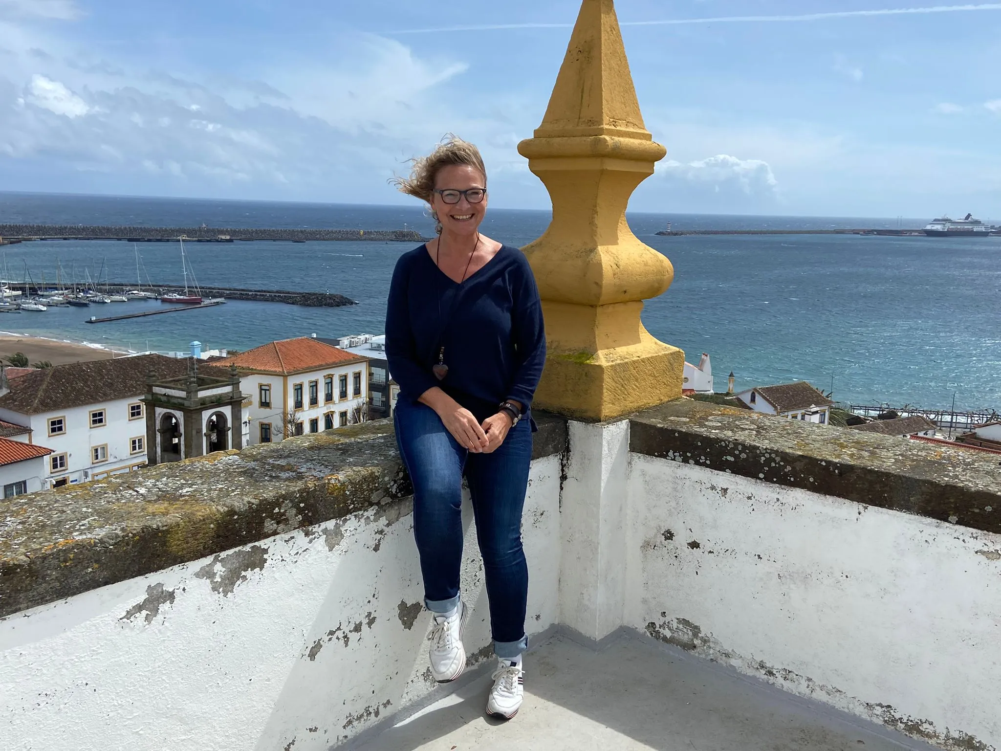 Blick von einem Hügel auf eine Stadt mit vielen Gebäuden, einem Hafen und Bergen im Hintergrund.