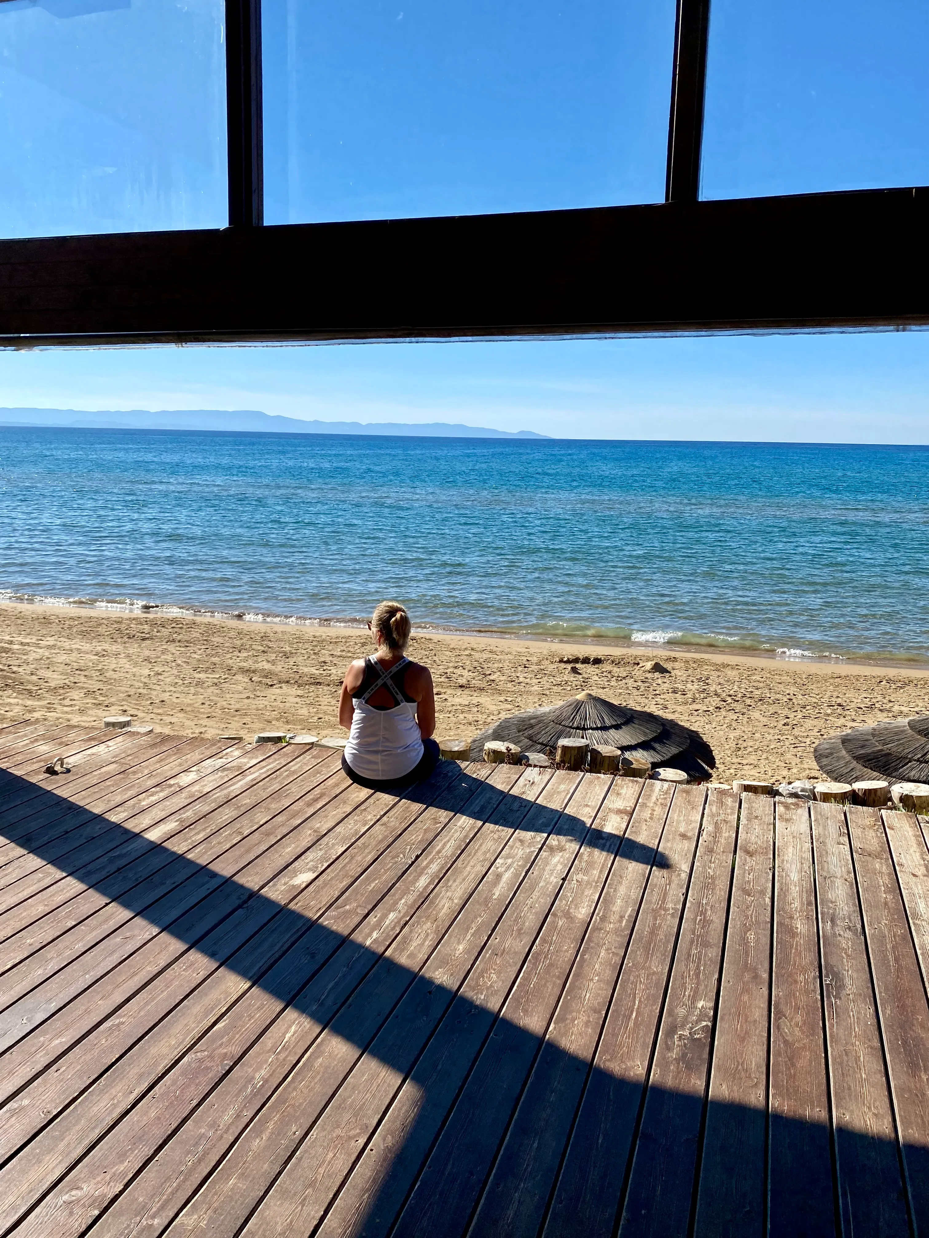 Frau sitzt auf einem Holzsteg am Strand