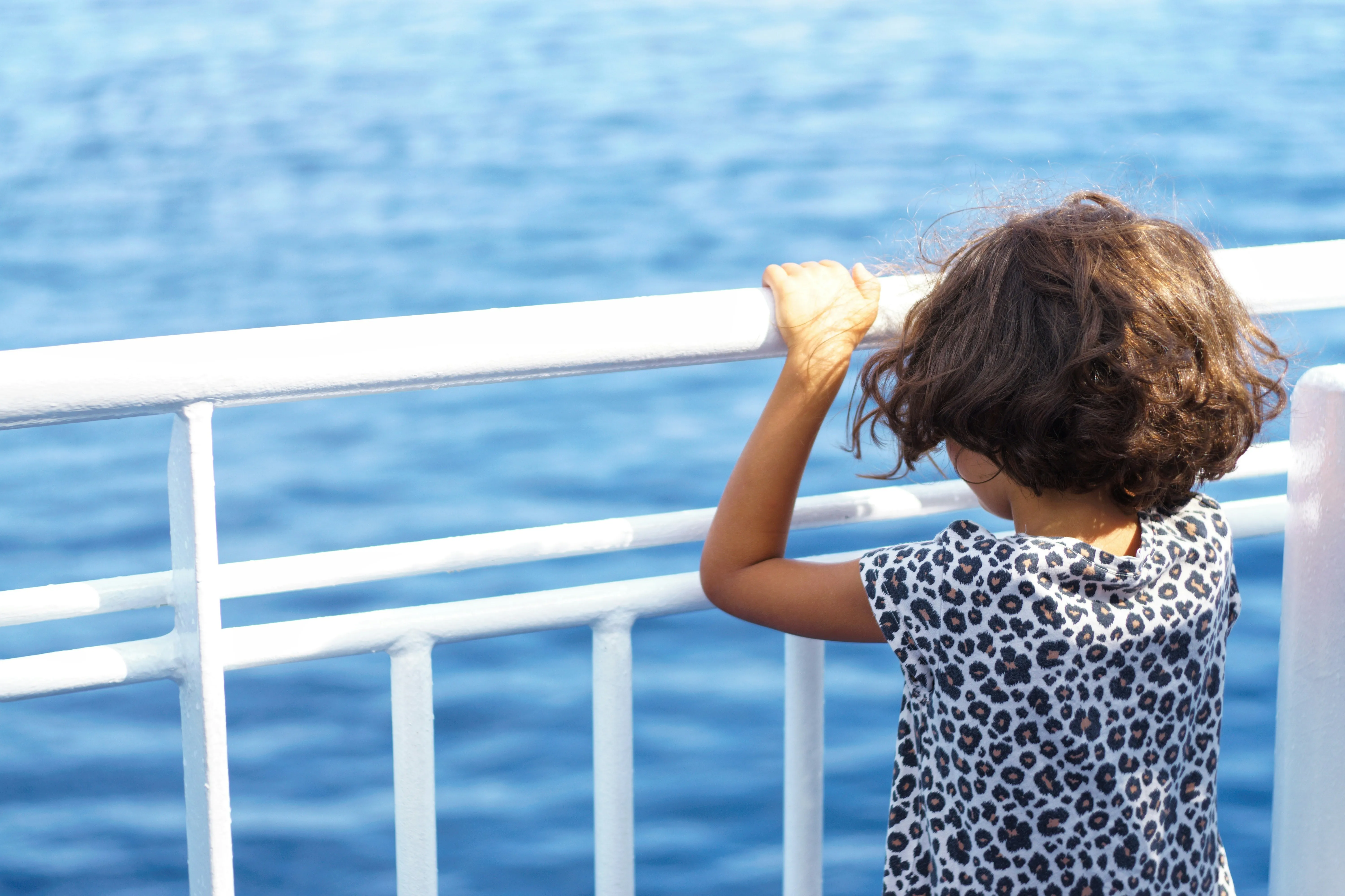 Kind steht an einer Reling mit Blick auf das Meer
