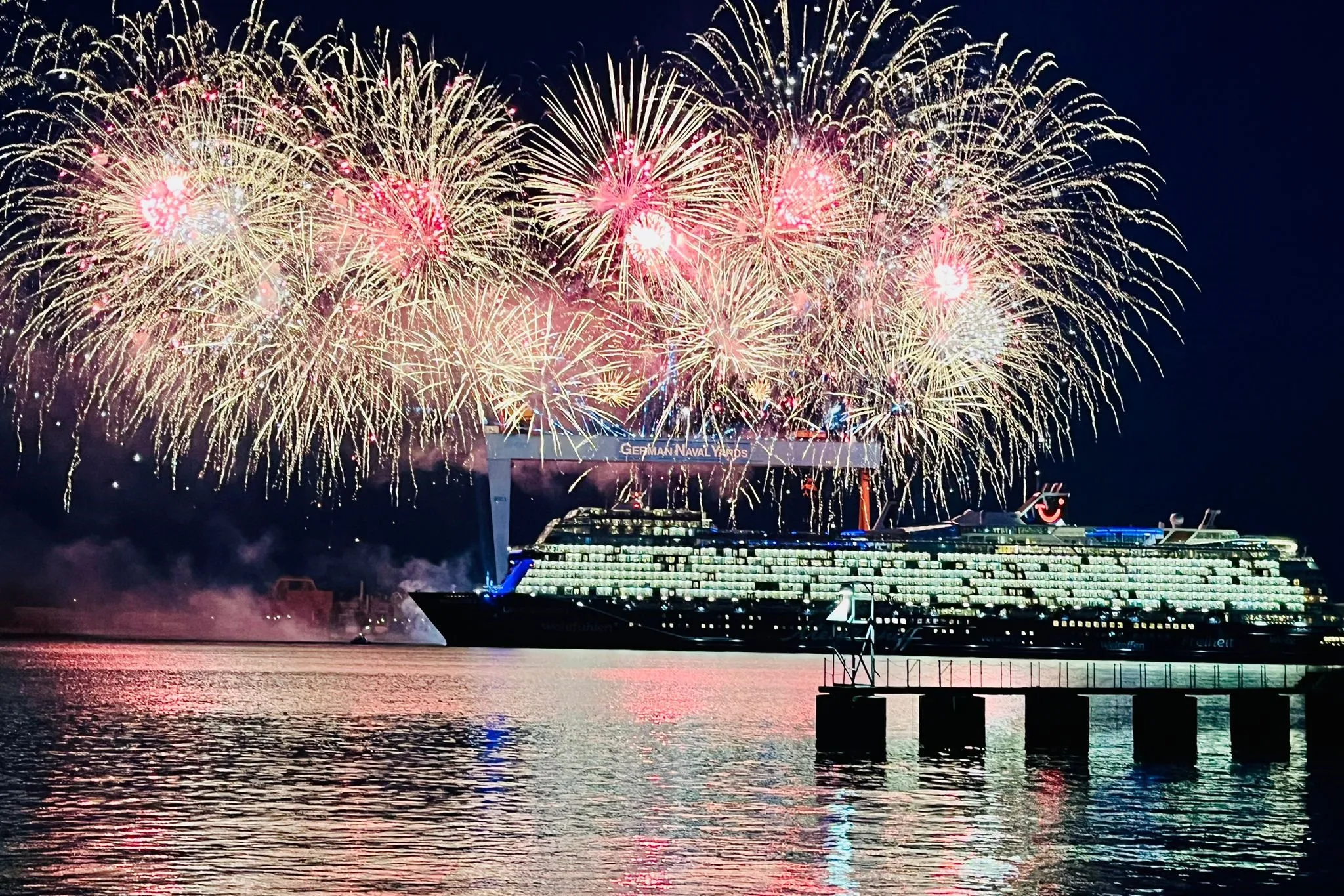 Kreuzfahrtschiff vor einem Kai mit großem Feuerwerk am Nachthimmel
