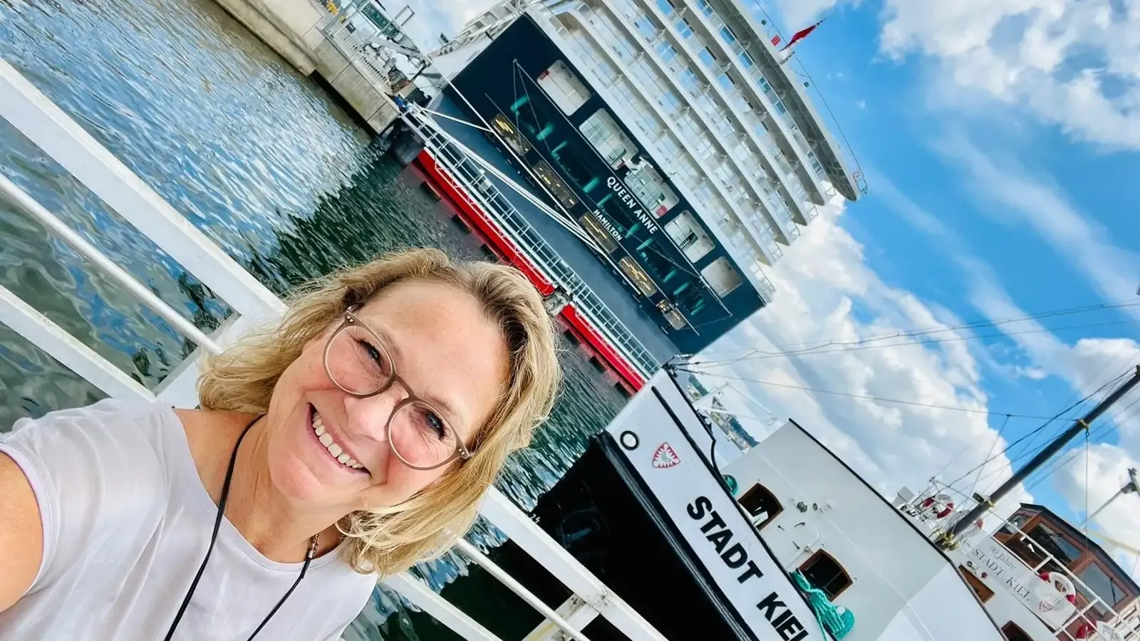 Blonde Frau mit Brille am Hafen vor einem Kreuzfahrtschiff