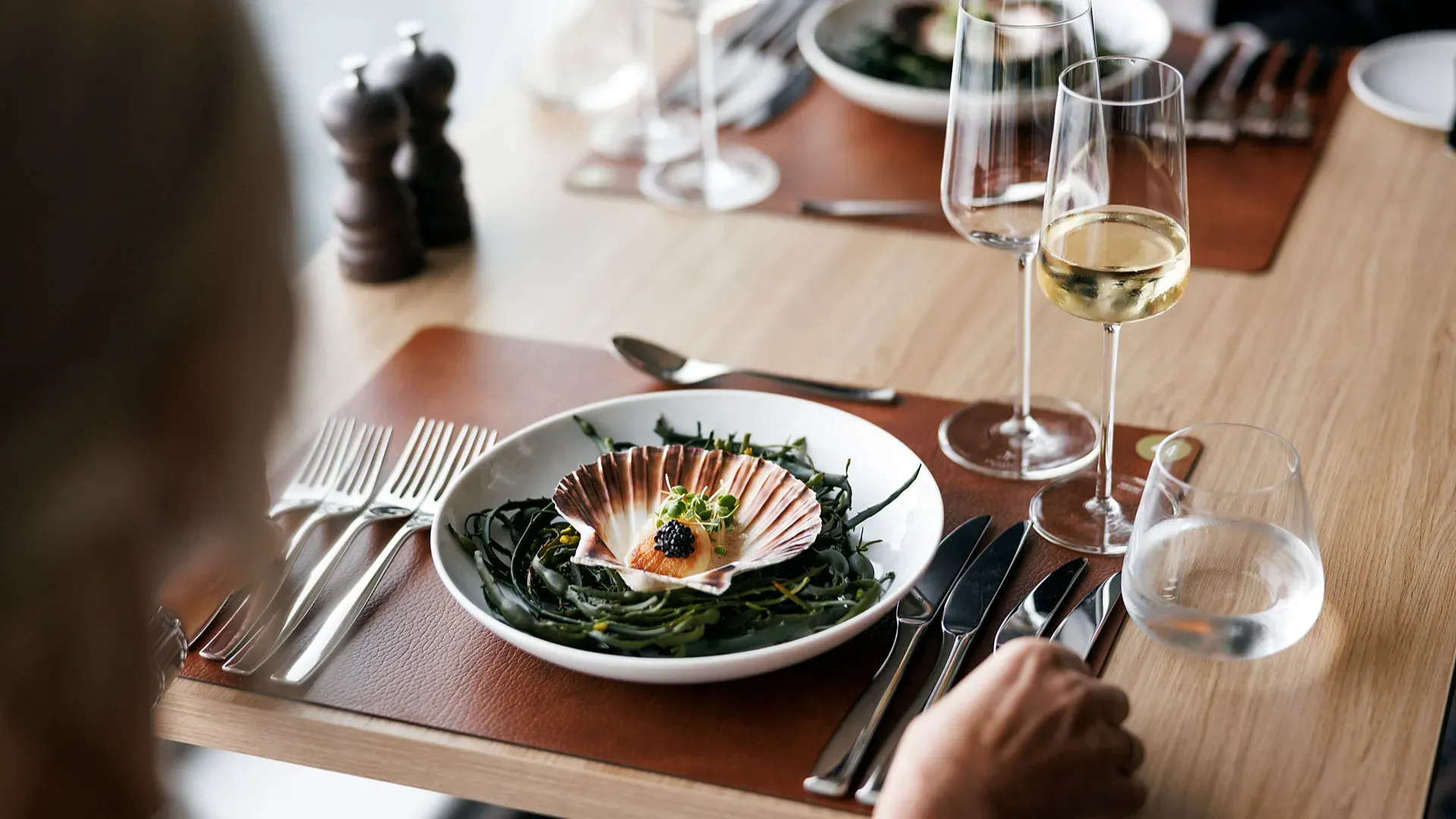 Zwei Personen sitzen an einem gedeckten Tisch in einem eleganten Restaurant mit gedämpfter Beleuchtung und roten Teppichböden