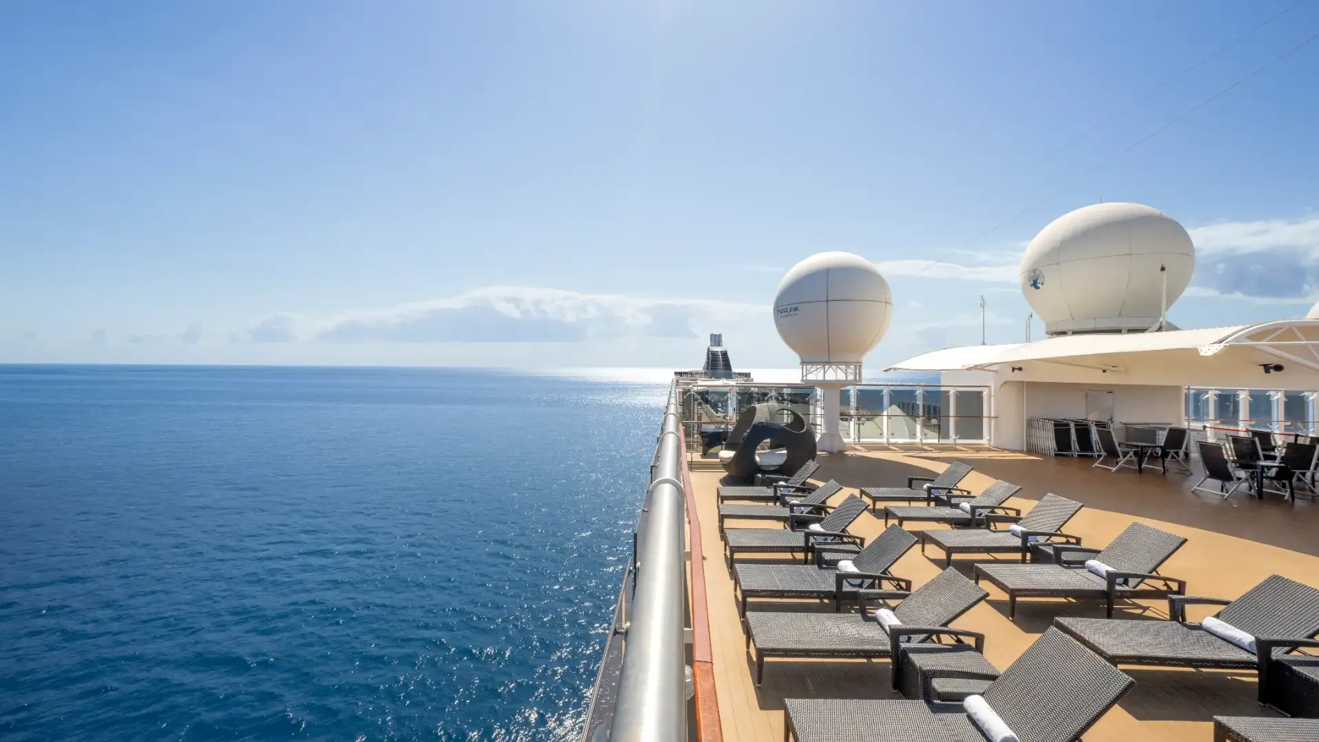Sonnendeck eines Kreuzfahrtschiffs mit Liegestühlen und zwei großen weißen Radarkuppeln über dem Meer