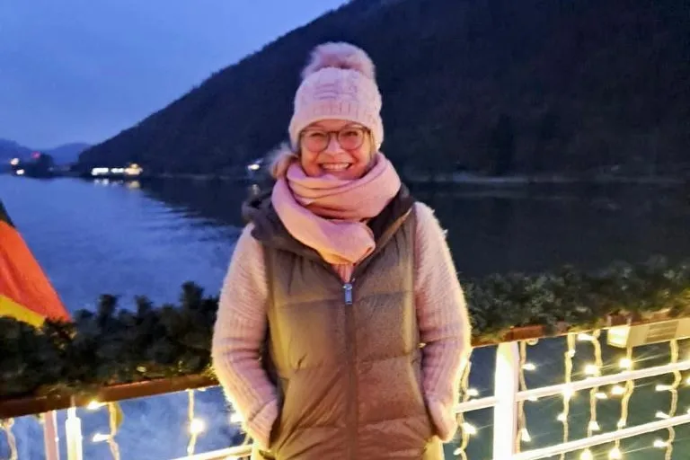 Frau mit Wintermütze und Jacke steht an der Reling von einem Flusskreuzfahrtschiff