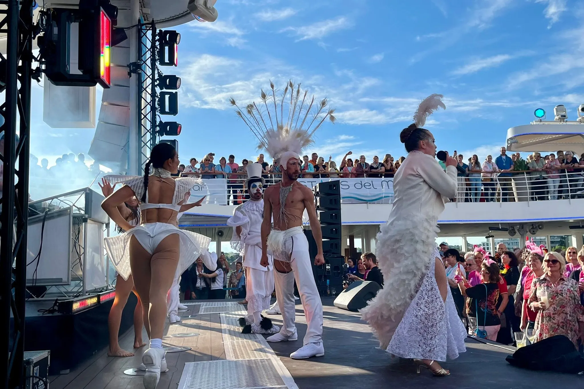 Mehrere Tänzer in weiß gekleidet tanzen auf Bühne, vor der viele Zuschauer stehen