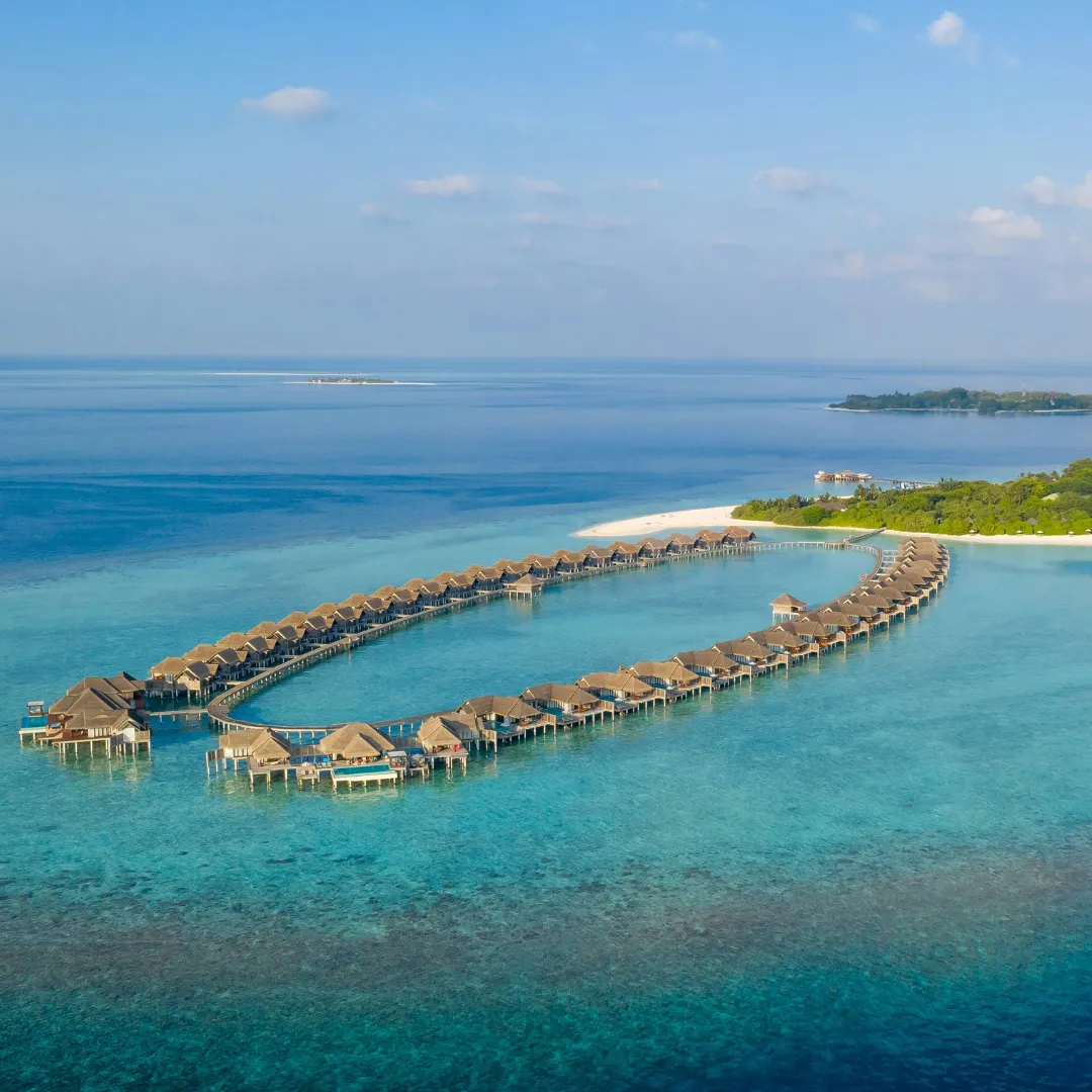 Luftaufnahme einer tropischen Insel mit zwei halbkreisförmigen Reihen von über Wasser gebauten Bungalows