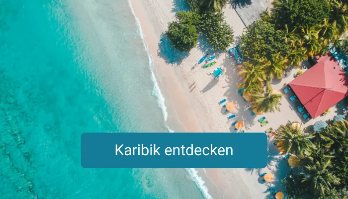 Luftaufnahme eines karibischen Strands mit türkisfarbenem Wasser, Palmen, Sonnenschirmen und einem roten Dach