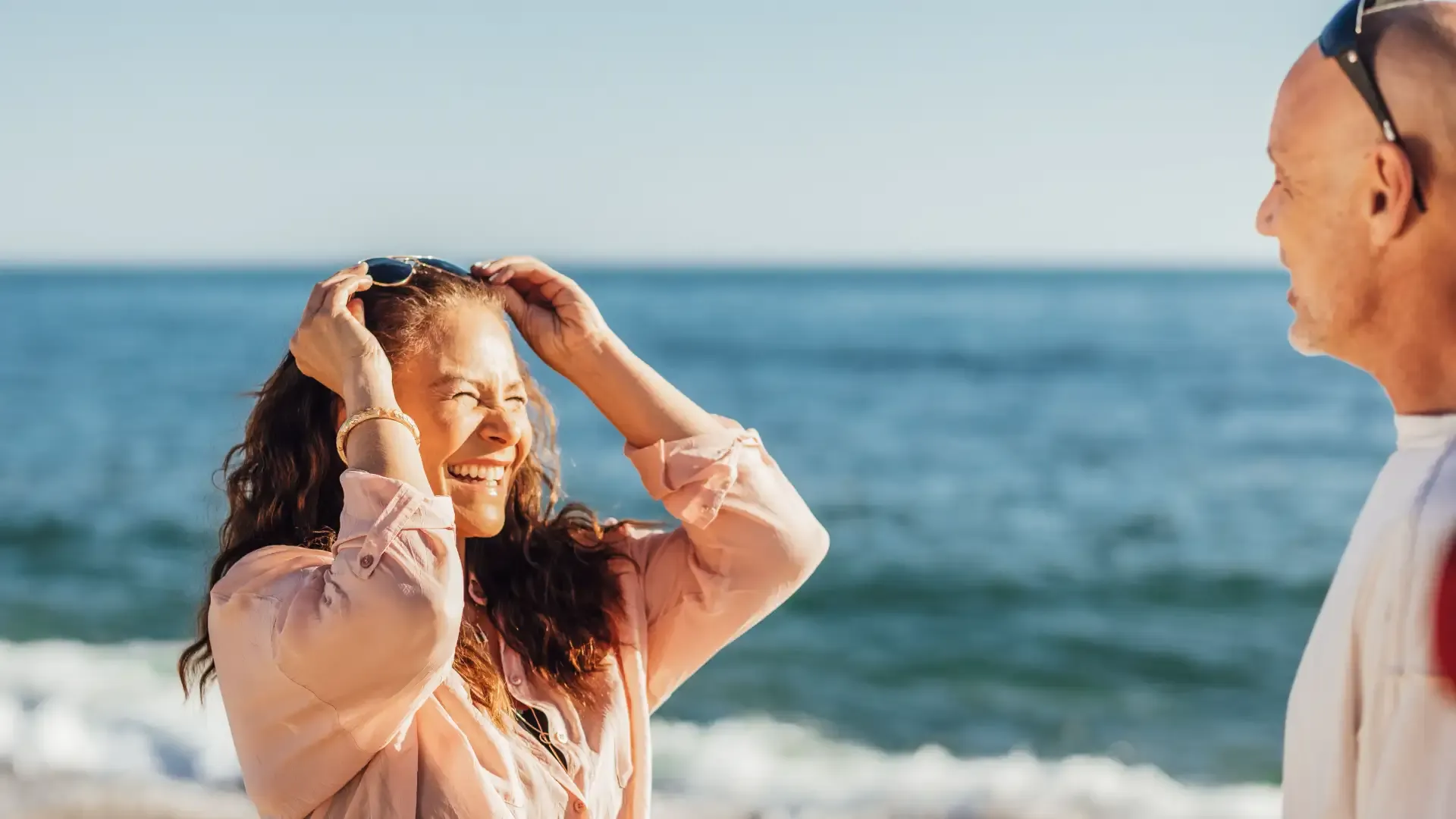 Frau am Strand, die ihre Sonnenbrille aufsetzt, im Hintergrund das Meer